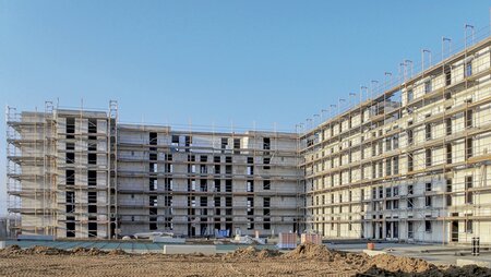 Rohbau eines mehrgeschossigen Gebäudes mit Kalksandsteinwänden und Baukran im Hintergrund