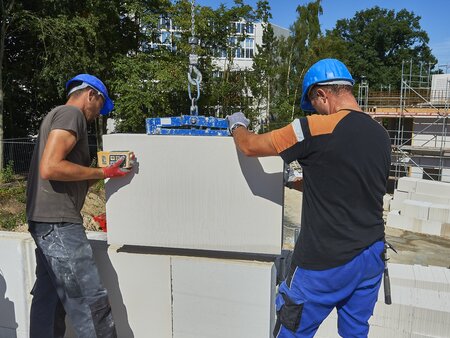 Mitarbeitende auf einer Baustelle beim Versetzen von Kalksandstein im Wohnungsbau