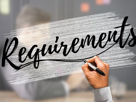 Hand schreibt das Wort „Requirements“ auf eine Glasfläche als Symbol für Anforderungen und Voraussetzungen.