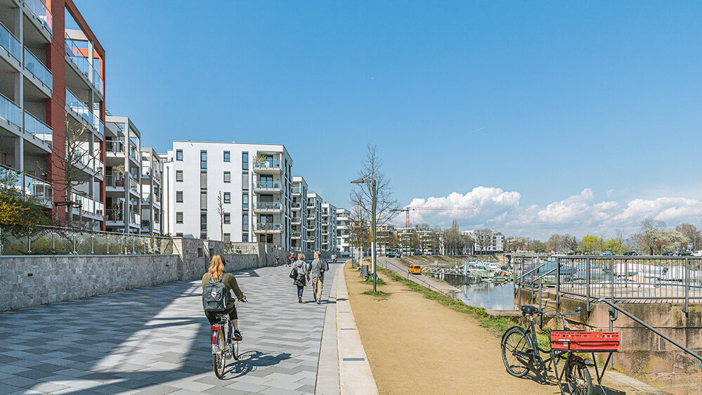 Uferpromenade am Mainzer Winterhafen mit Wohngebäuden, Radfahrerin, Fußgängern und Blick auf das Hafenbecken
